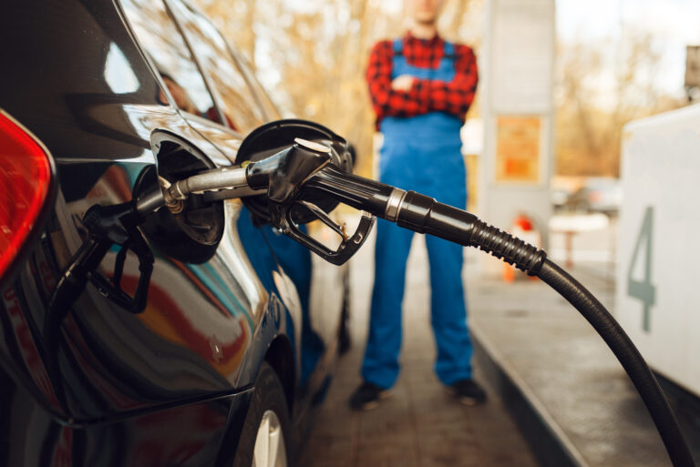 Male worker in uniform fuels vehicle, gas station