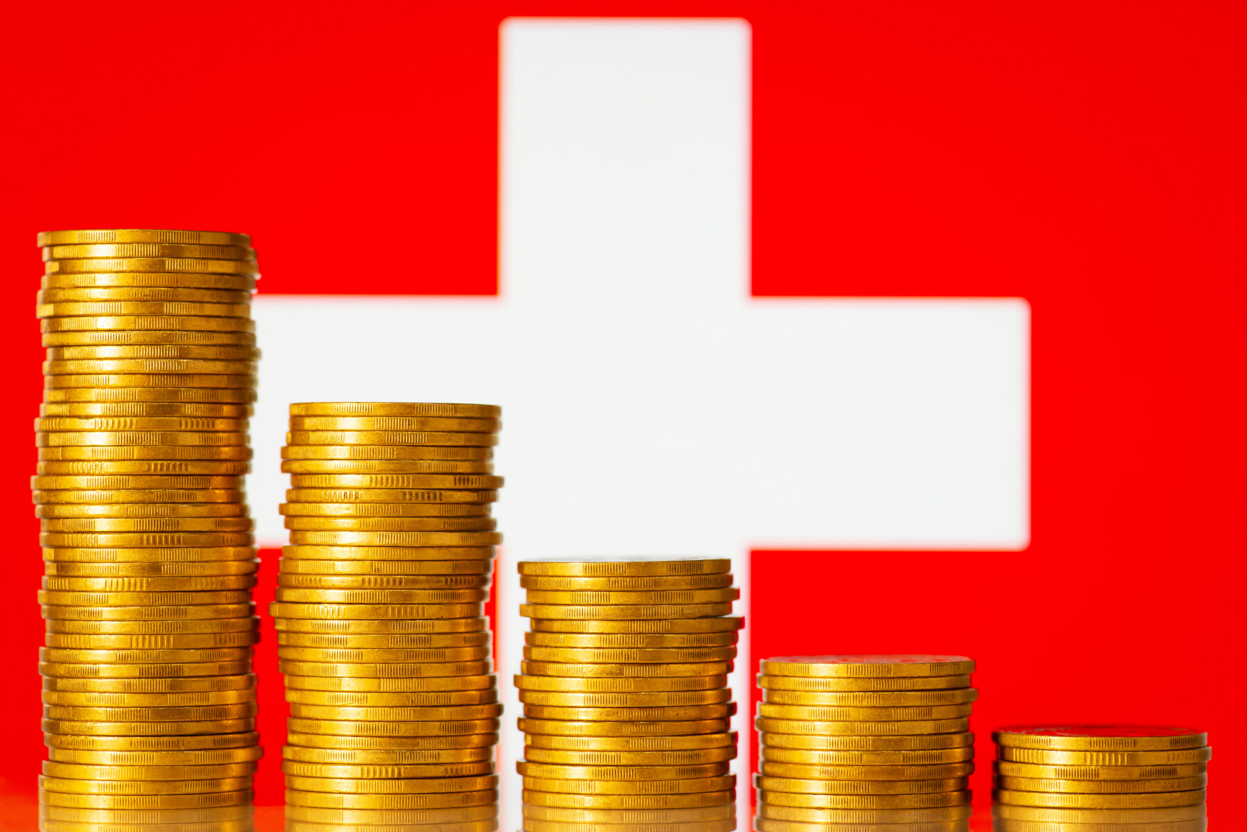 Problems in economy of Switzerland concept. Downcomming graph made of gold coins stacks with flag of Switzerland on the background
