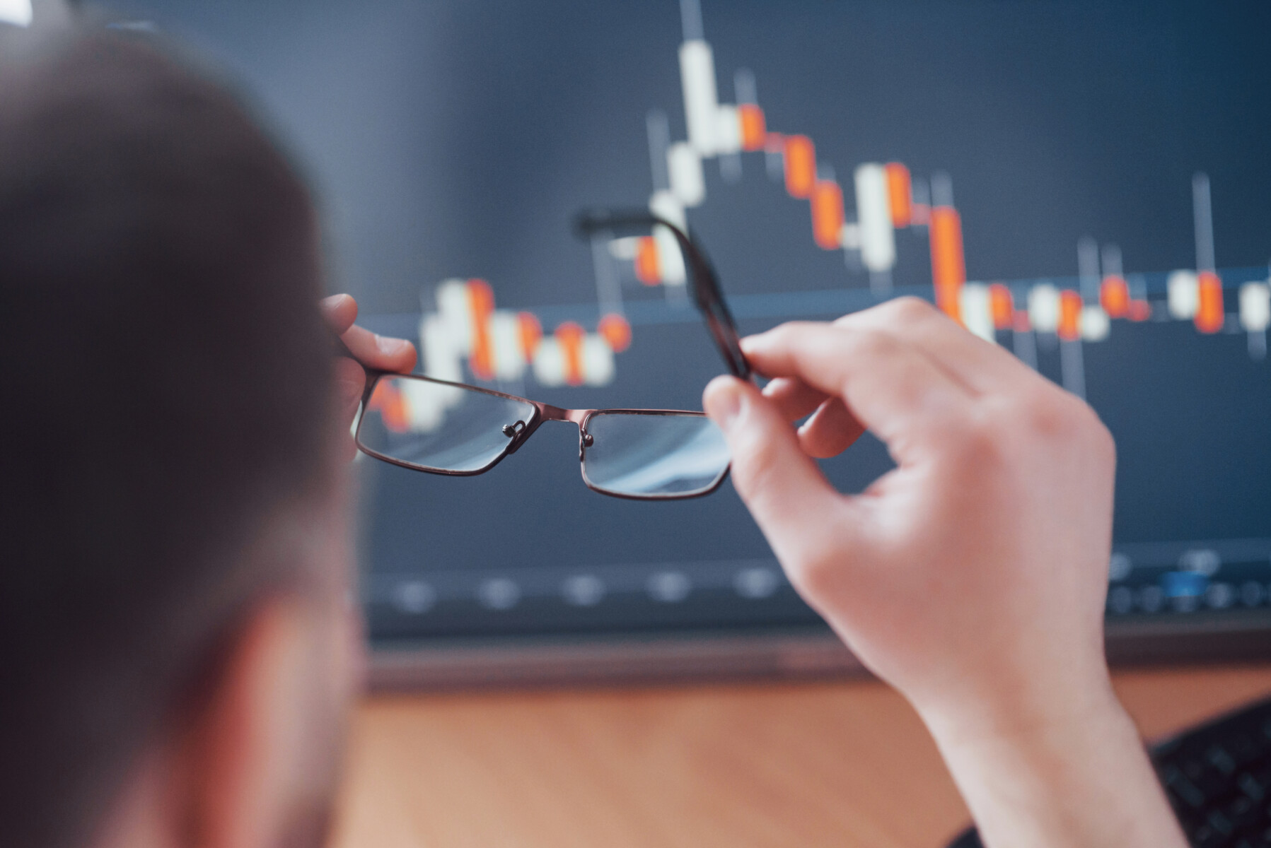 Analyzing data. Close up of a young businessman who holds glasses and looks at the gff while working in a creative office