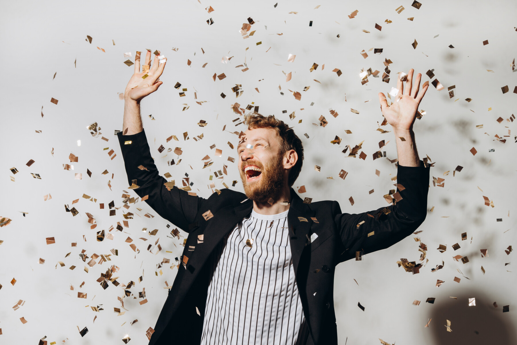 Concept of celebration and victory. Stylish young man isolated on white background under glittering confetti.