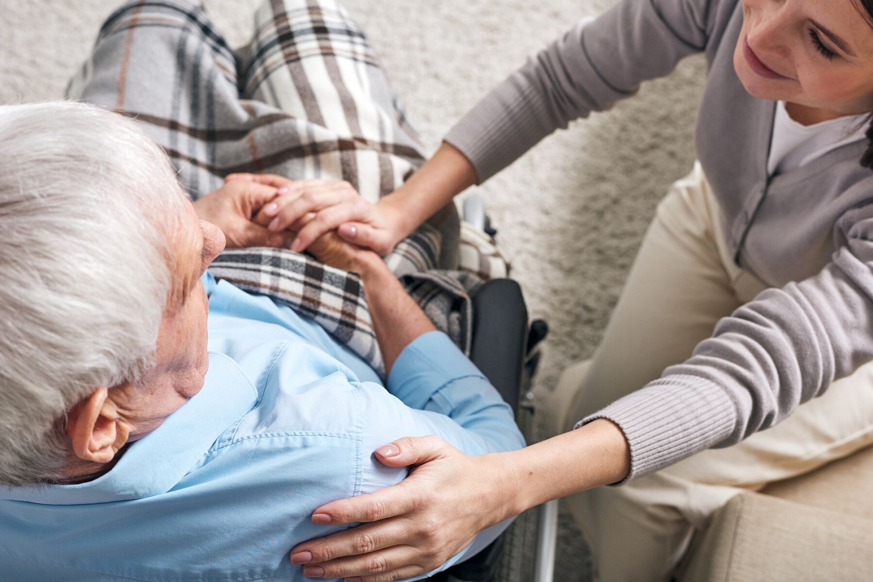 young-supportive-female-caregiver-sitting-by-senior-man-wheelchair-keeping-her-hand-his-shoulder-while-comforting-him