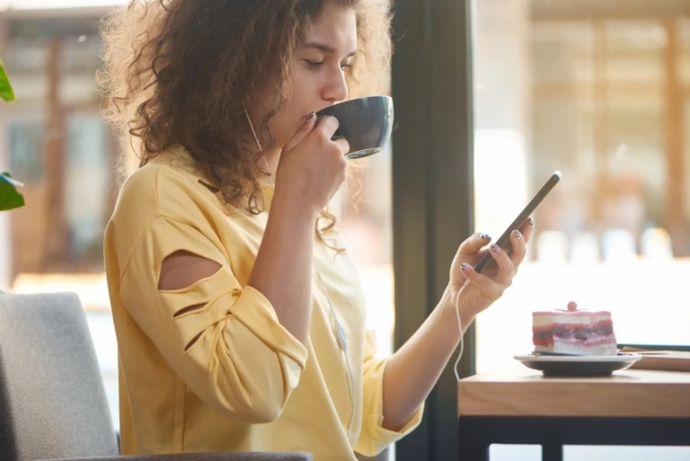 Curly girl relaxing drinking coffee cafe using smartphone