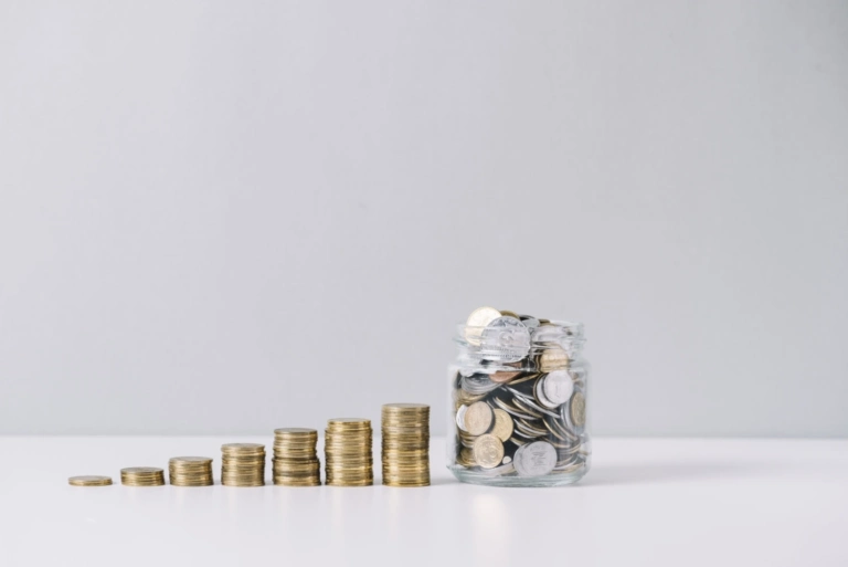 Glass jar full money front decreasing stacked coins against white background