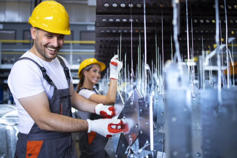Factory employees with yellow hardhats inspecting metal parts automobile factory