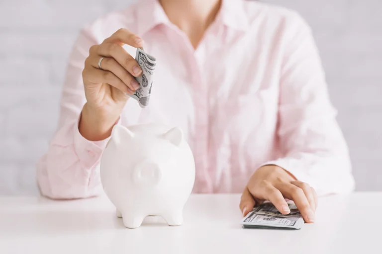 Close up woman inserting hundred dollar currency white piggybank