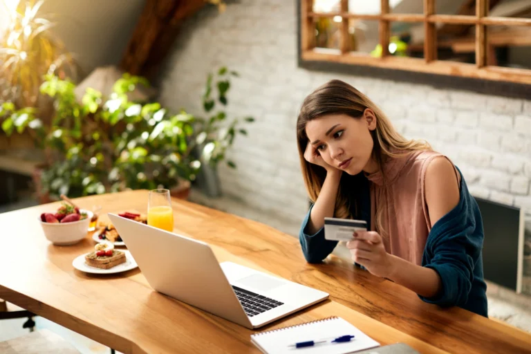 Young woman feeling sad while checking her online bank account laptop home